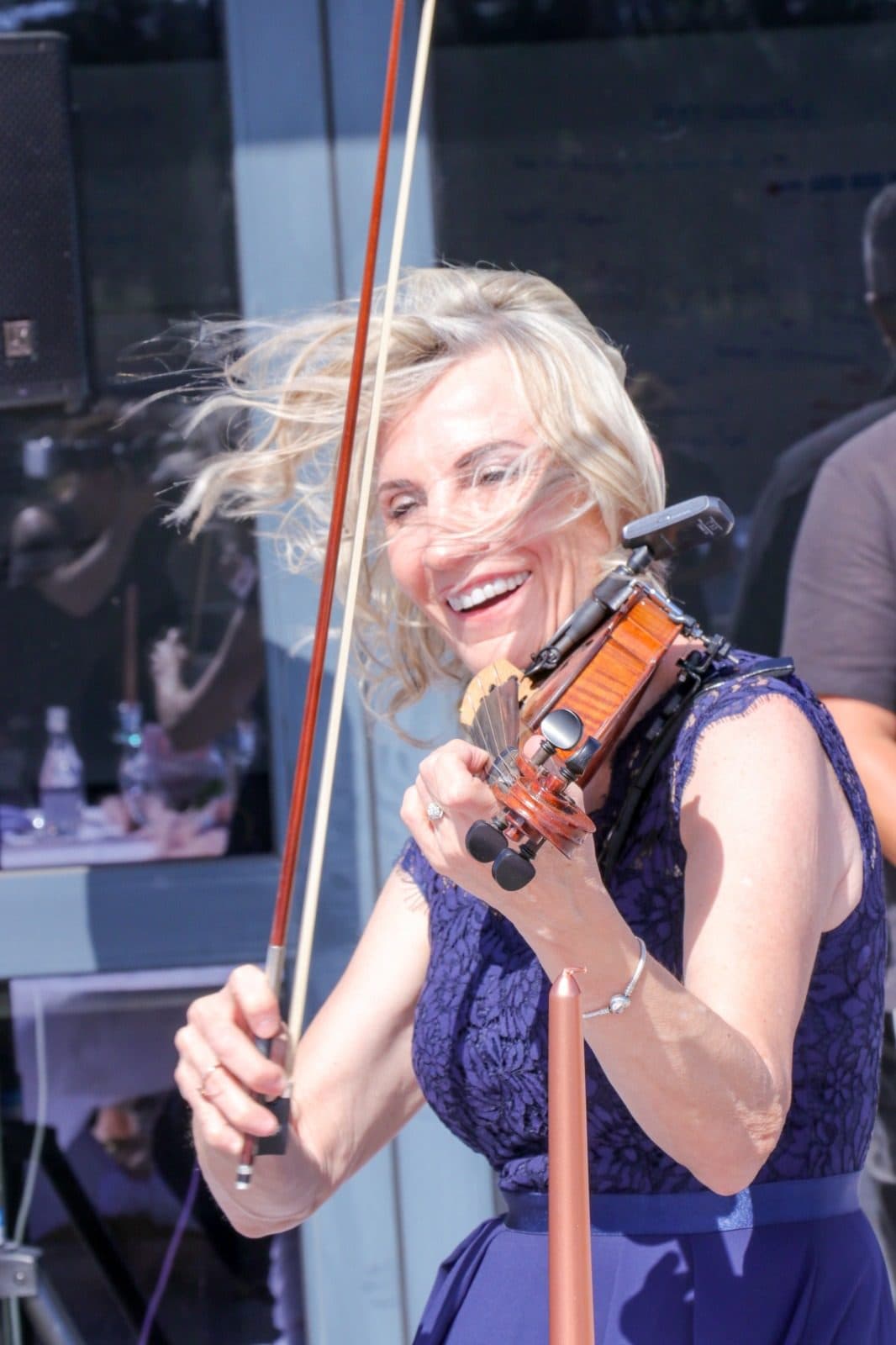 Esmé Bergh laughing with her violin and bow raised, her hair caught by the wind
