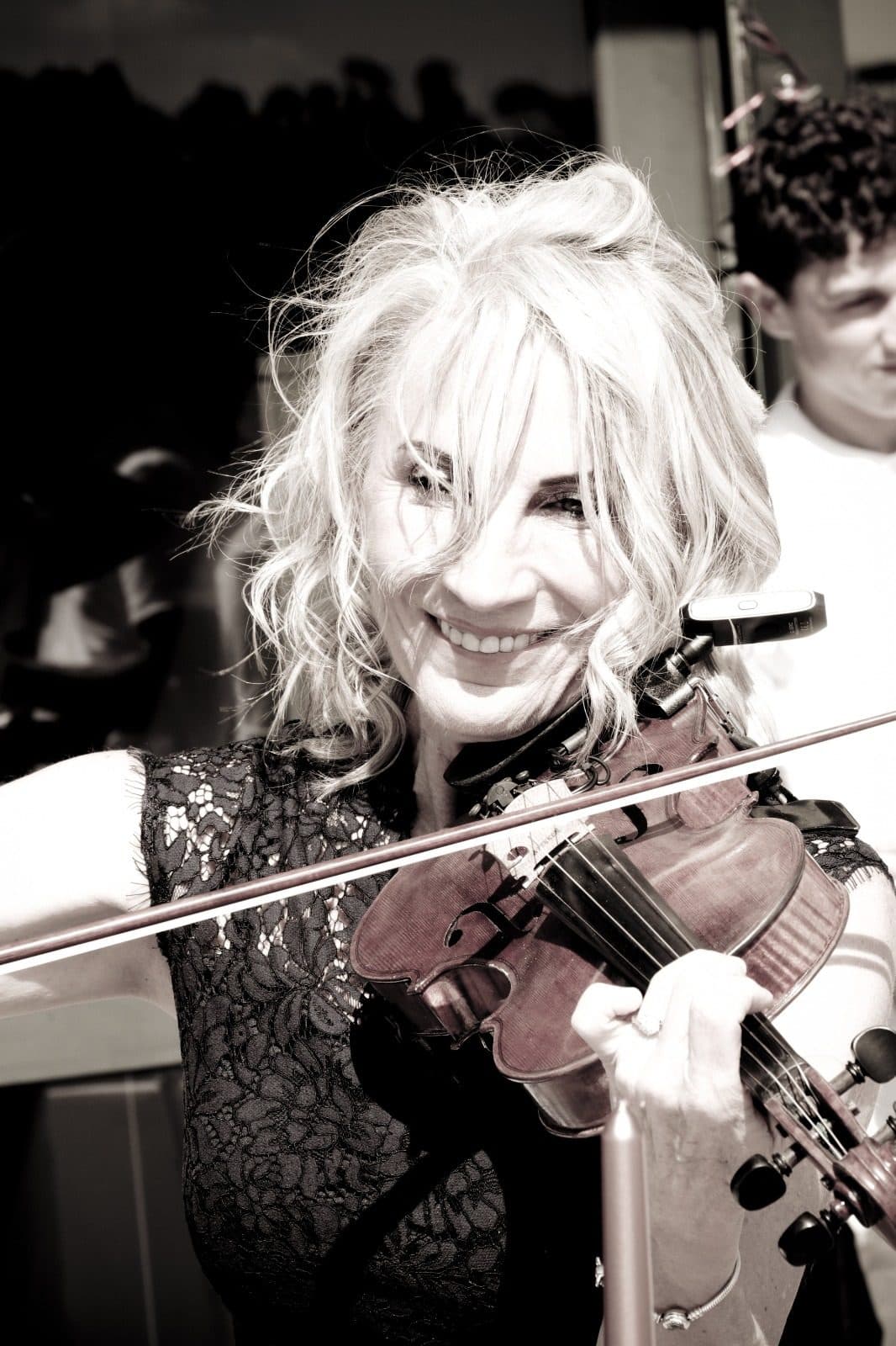 A black and white photograph of Esmé Bergh smiling while she plays the violin